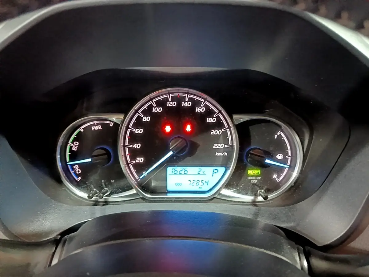 Vue rapprochée du tableau de bord de la Toyota Yaris hybride blanche, affichant la vitesse, jauge et indicateurs lumineux.