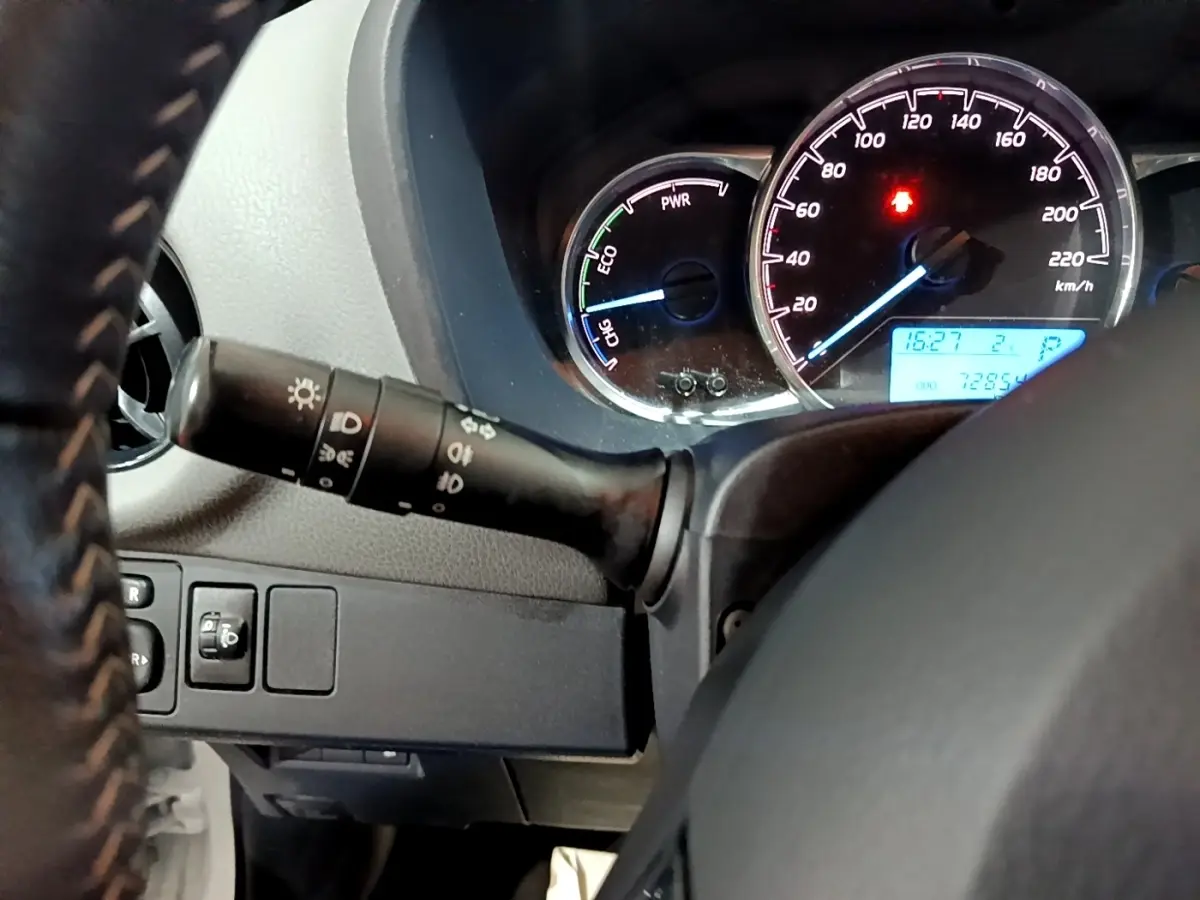 Gros plan sur le tableau de bord et le volant cuir noir de la Toyota Yaris hybride, avec compteurs éclairés et commandes lumineuses.