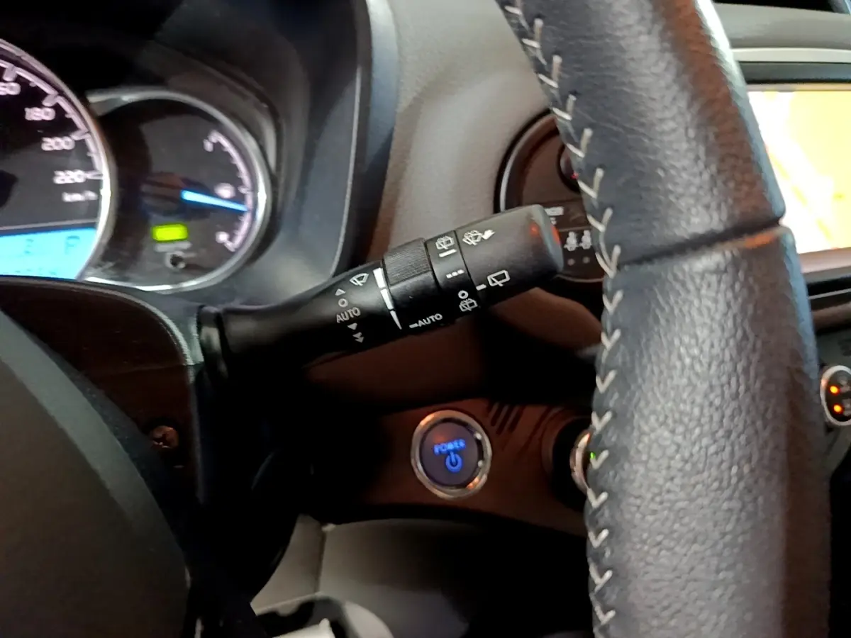 Gros plan sur le volant cuir et le bouton démarrage bleu de la Toyota Yaris 1.5 Hybride, tableau de bord partiellement visible.