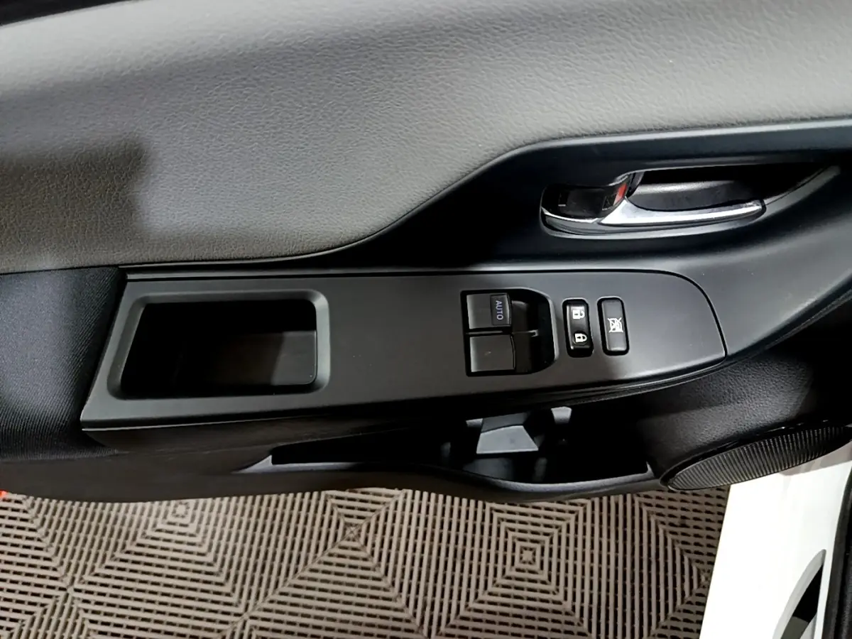 Gros plan sur la commande de lève-vitres et la poignée intérieure côté conducteur d'une Toyota Yaris blanche.