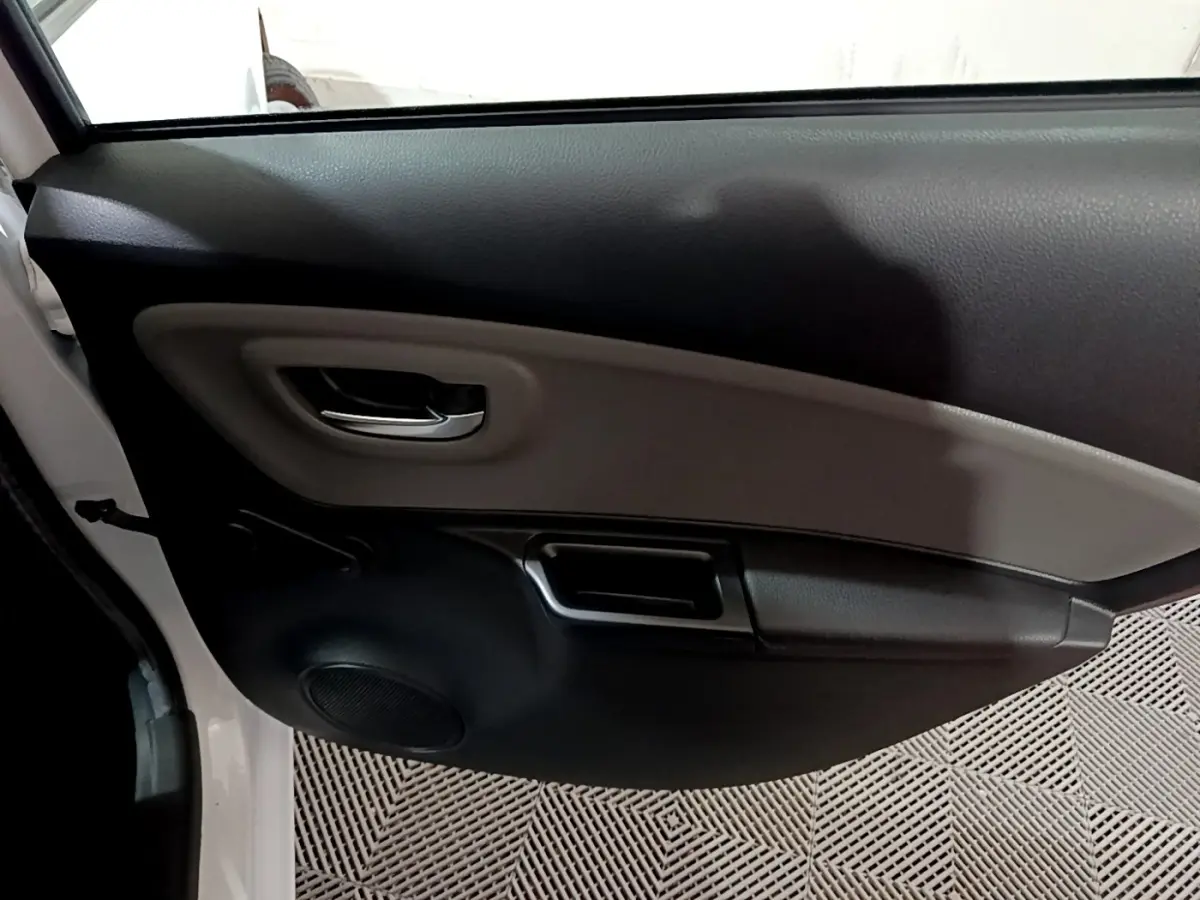 Vue intérieure de la porte avant gauche blanche d'une Toyota Yaris 1.5 Hybride 2020 avec poignée chrome et haut-parleur intégré.