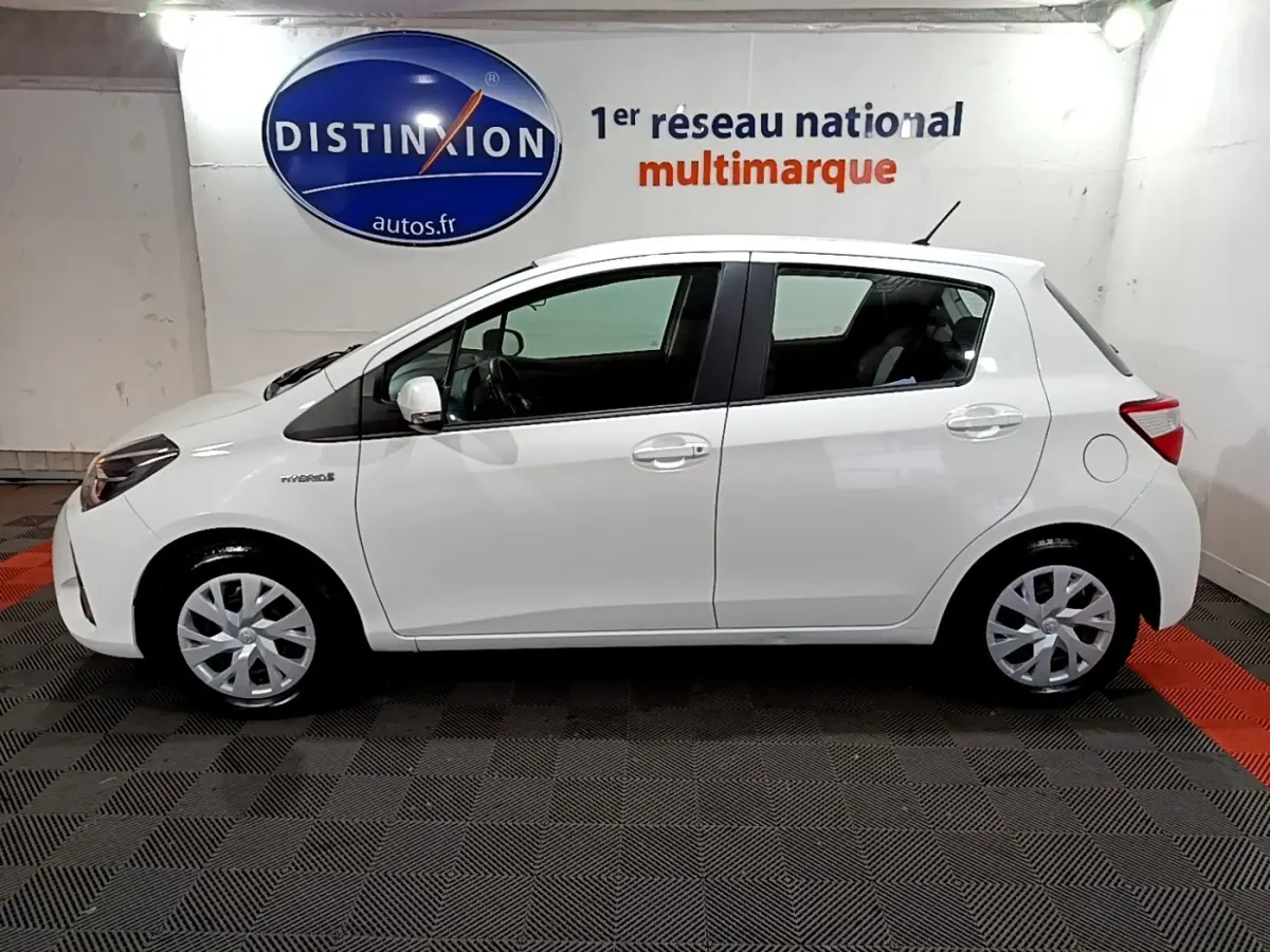 Profil côté gauche d'une Toyota Yaris 1.5 Hybride blanche, avec jantes alliage et logo hybride visible sur l'aile avant.