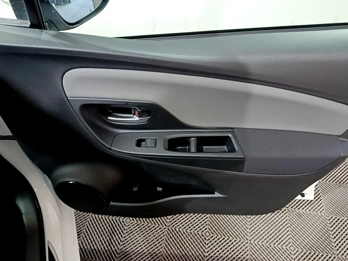 Vue intérieure du panneau de porte avant gauche de la Toyota Yaris blanche, avec commandes de vitres et poignée noire.