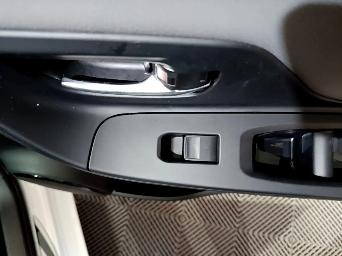 Poignée de porte intérieure chromée et commandes de lève-vitre sur la portière avant gauche d'une Toyota Yaris blanche.