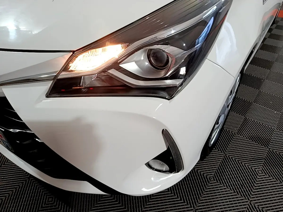 Gros plan sur l'avant droit blanc de la Toyota Yaris 1.5 Hybride, phare allumé et antibrouillard visible.