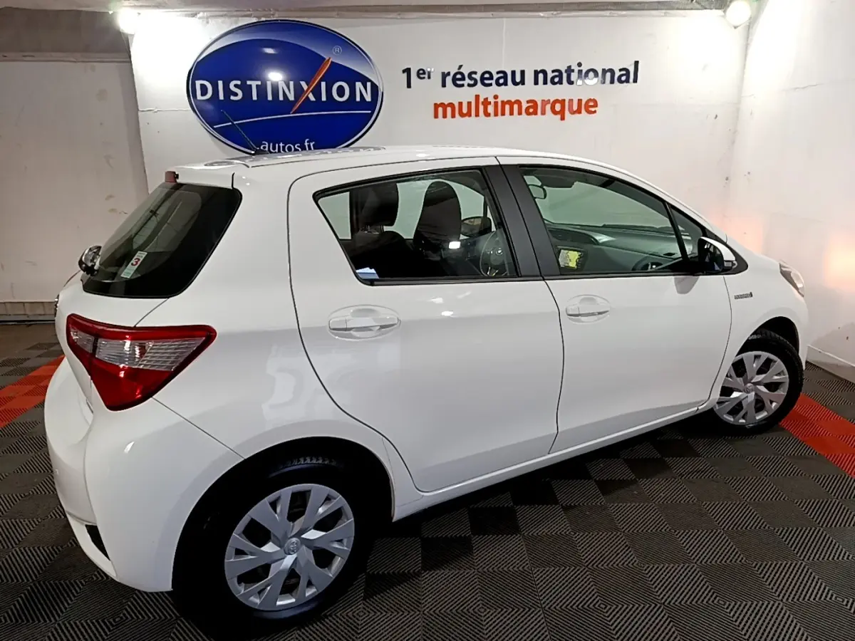 Vue côté droit d'une Toyota Yaris blanche 1.5 Hybride 2020 en intérieur avec jantes alliage et vitres teintées.