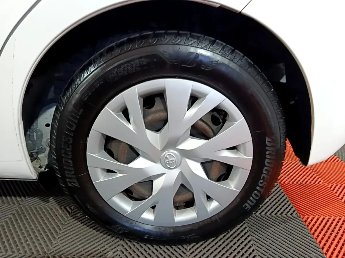 Gros plan sur la roue avant droite d'une Toyota Yaris blanche, avec enjoliveur argenté et pneu Bridgestone.
