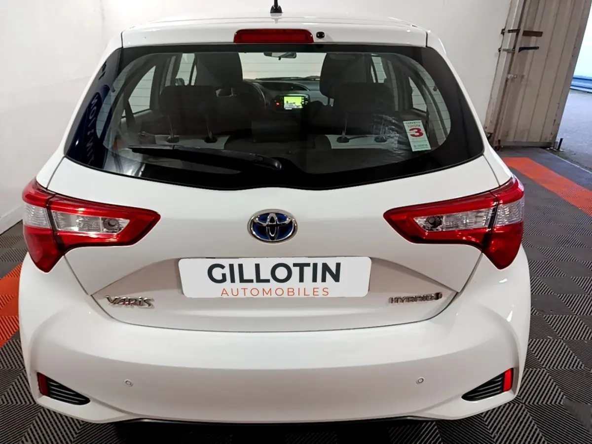 Vue arrière d'une Toyota Yaris blanche 1.5 Hybride 2020 avec feux distinctifs et logo Toyota visible.