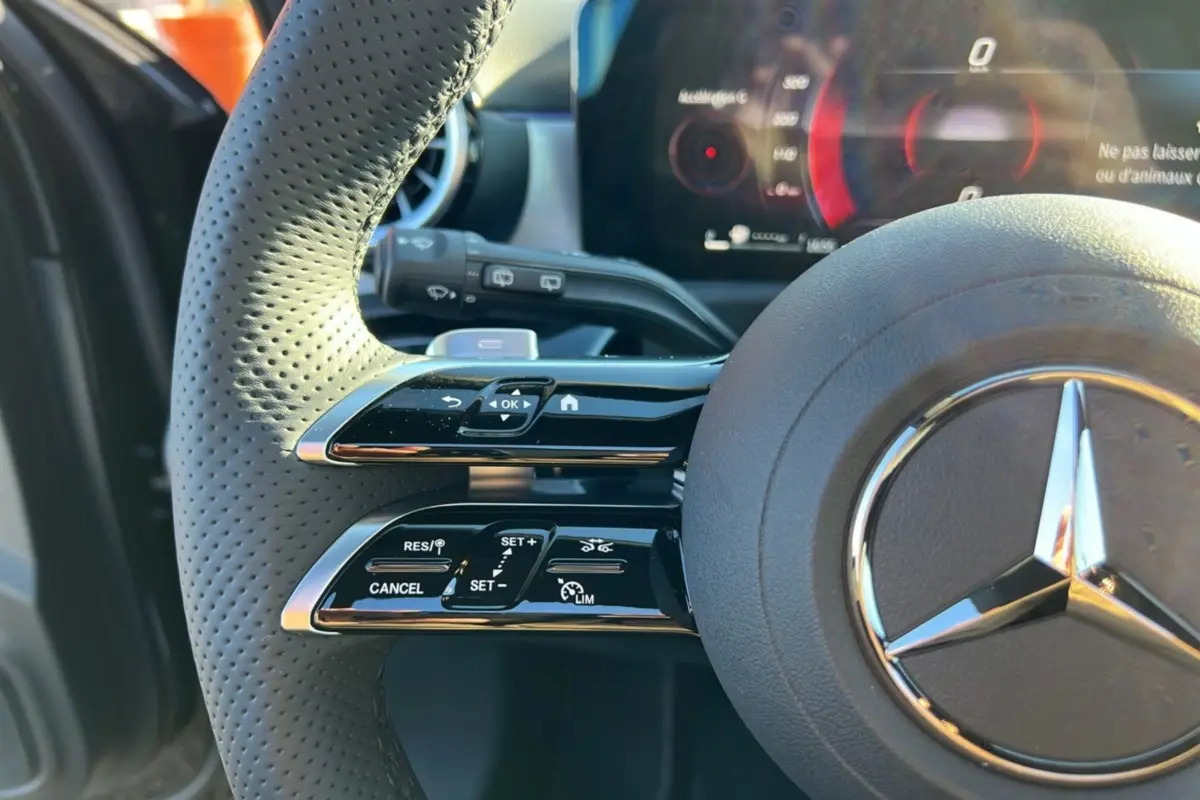 Gros plan sur le volant cuir perforé noir de la Mercedes Classe A 200D, avec commandes multifonctions et tableau de bord numérique.