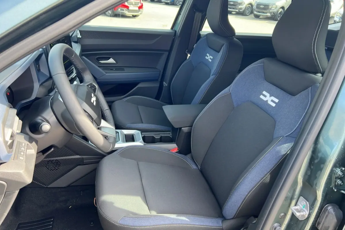 Vue intérieure côté conducteur du Dacia Bigster Hybrid 155 Expression Plus avec sièges bi-matière noirs et bleus et accoudoir central.