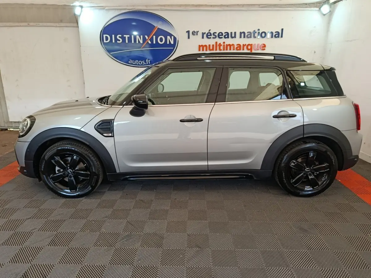 Vue de profil côté gauche d'une MINI Countryman gris foncé avec jantes noires et toit noir dans un showroom.