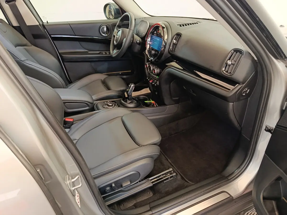 Intérieur côté passager de la MINI Countryman gris foncé 2023, avec tableau de bord et sièges en cuir noir.