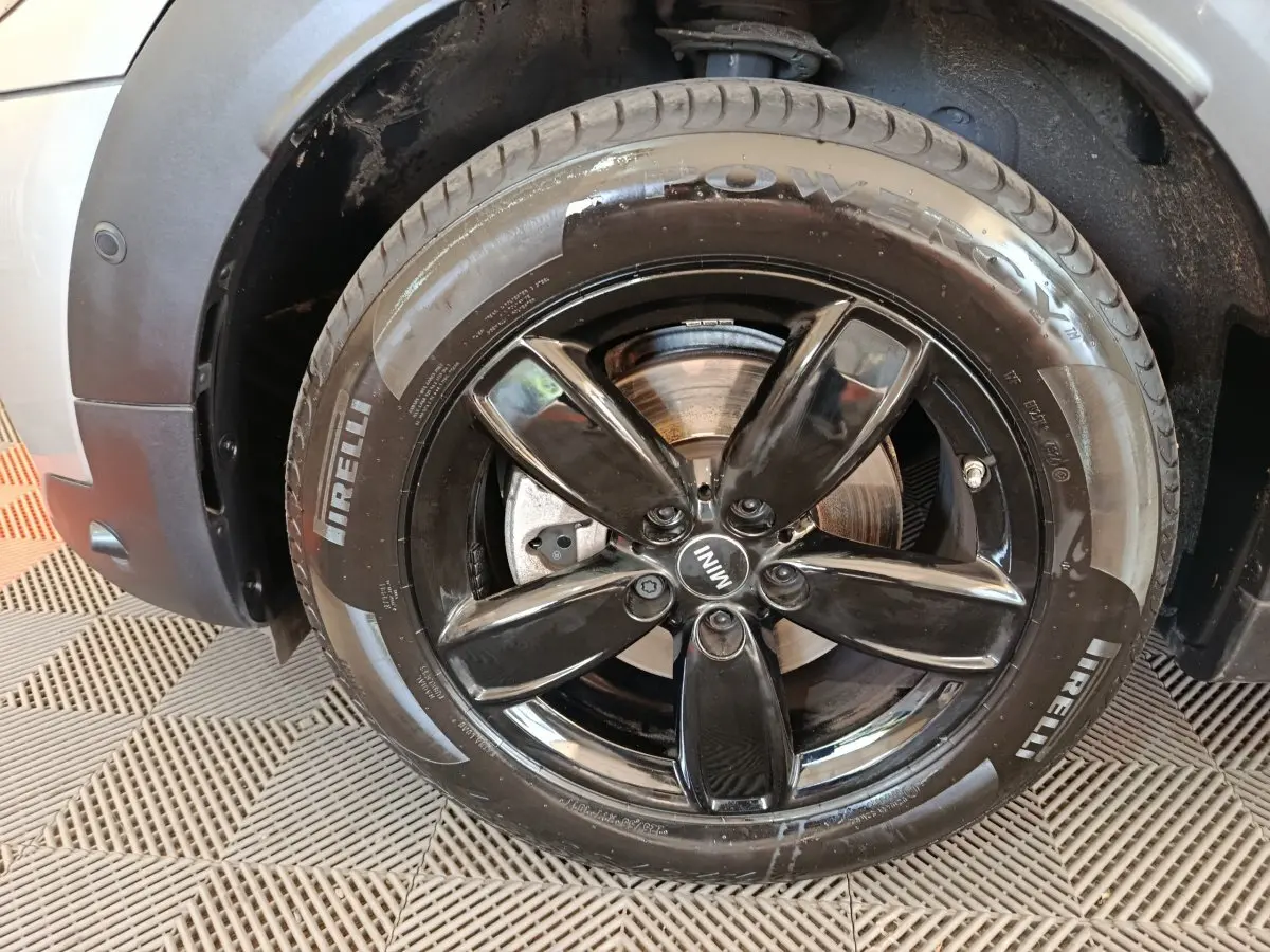 Gros plan sur la roue avant gauche noire brillante d'une MINI Countryman gris foncé avec pneu Pirelli visible.