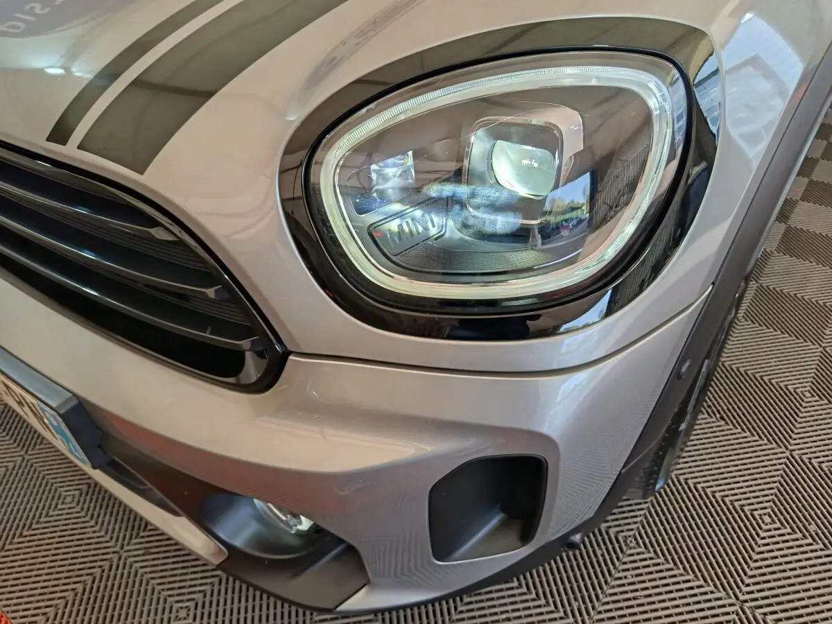 Gros plan sur le phare avant droit et la calandre d’un MINI Countryman gris foncé, détails noirs contrastants visibles.