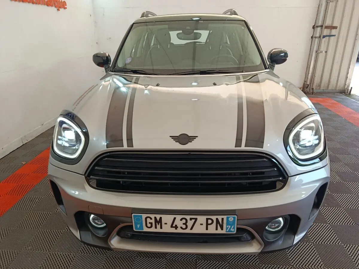 Vue avant d'une MINI Countryman gris foncé avec bandes noires sur le capot et phares LED allumés.
