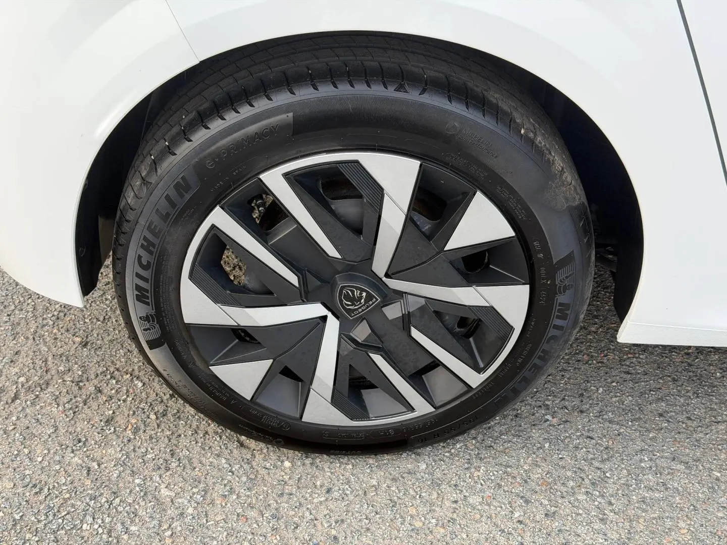 Gros plan sur la roue avant gauche d'une Peugeot 208 blanche, avec jante noire et argentée au design géométrique.