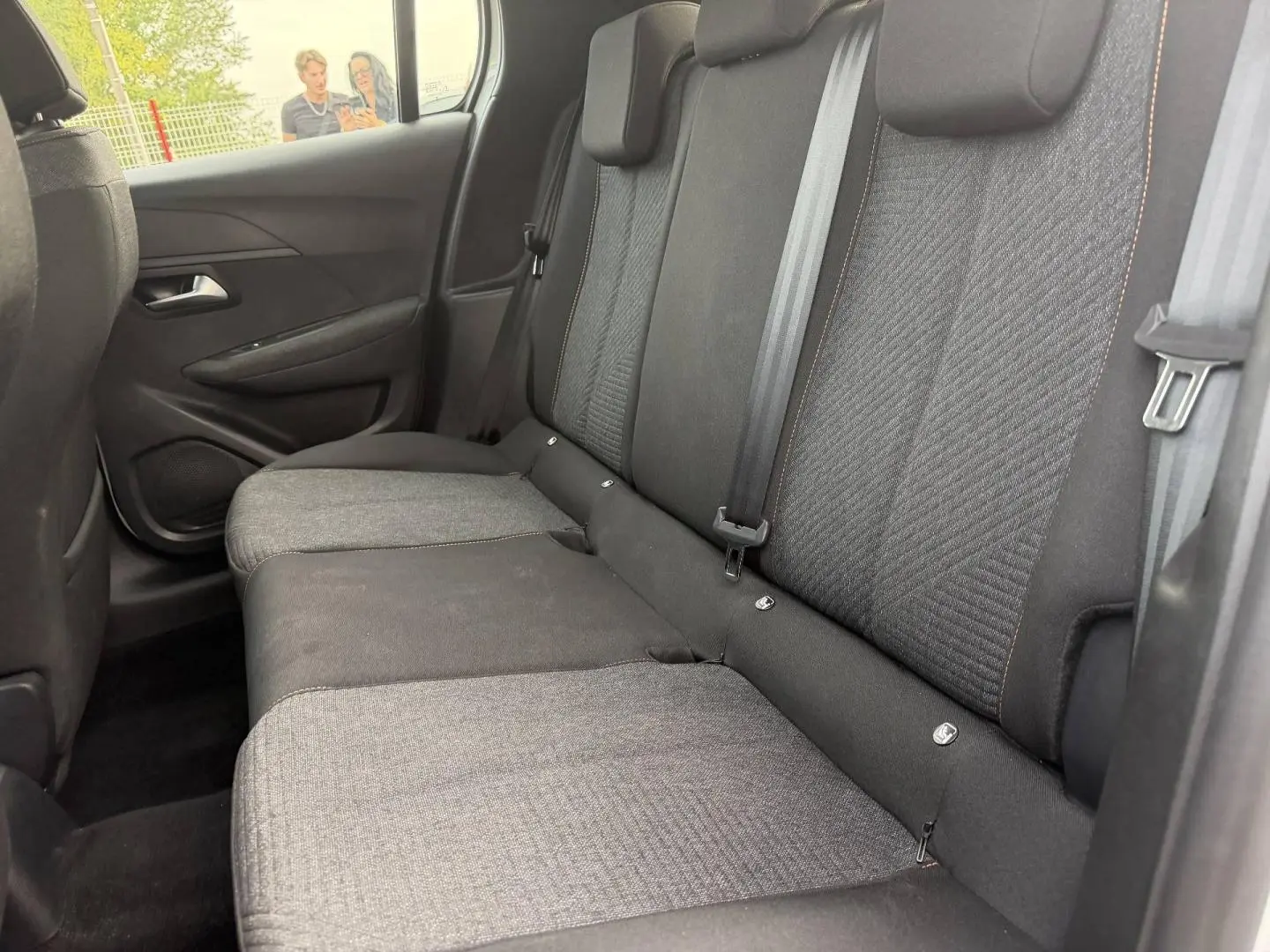 Vue intérieure côté droit sur la banquette arrière tissu gris foncé avec surpiqûres orange de la Peugeot 208 blanche.