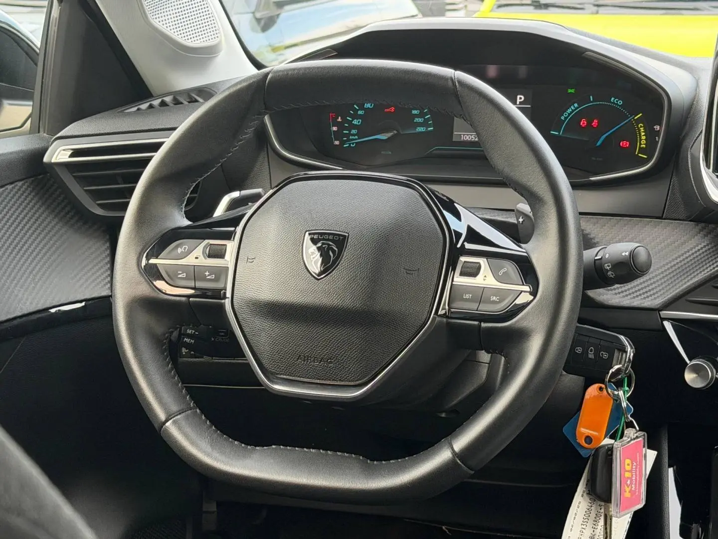 Vue intérieure centrée sur le volant noir de la Peugeot 208 1.2 Hybrid 110ch avec tableau de bord numérique allumé.