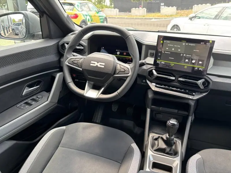 Vue intérieure côté conducteur du Dacia Bigster blanc 2025, volant multifonction, écran tactile et levier de vitesse manuel visibles.