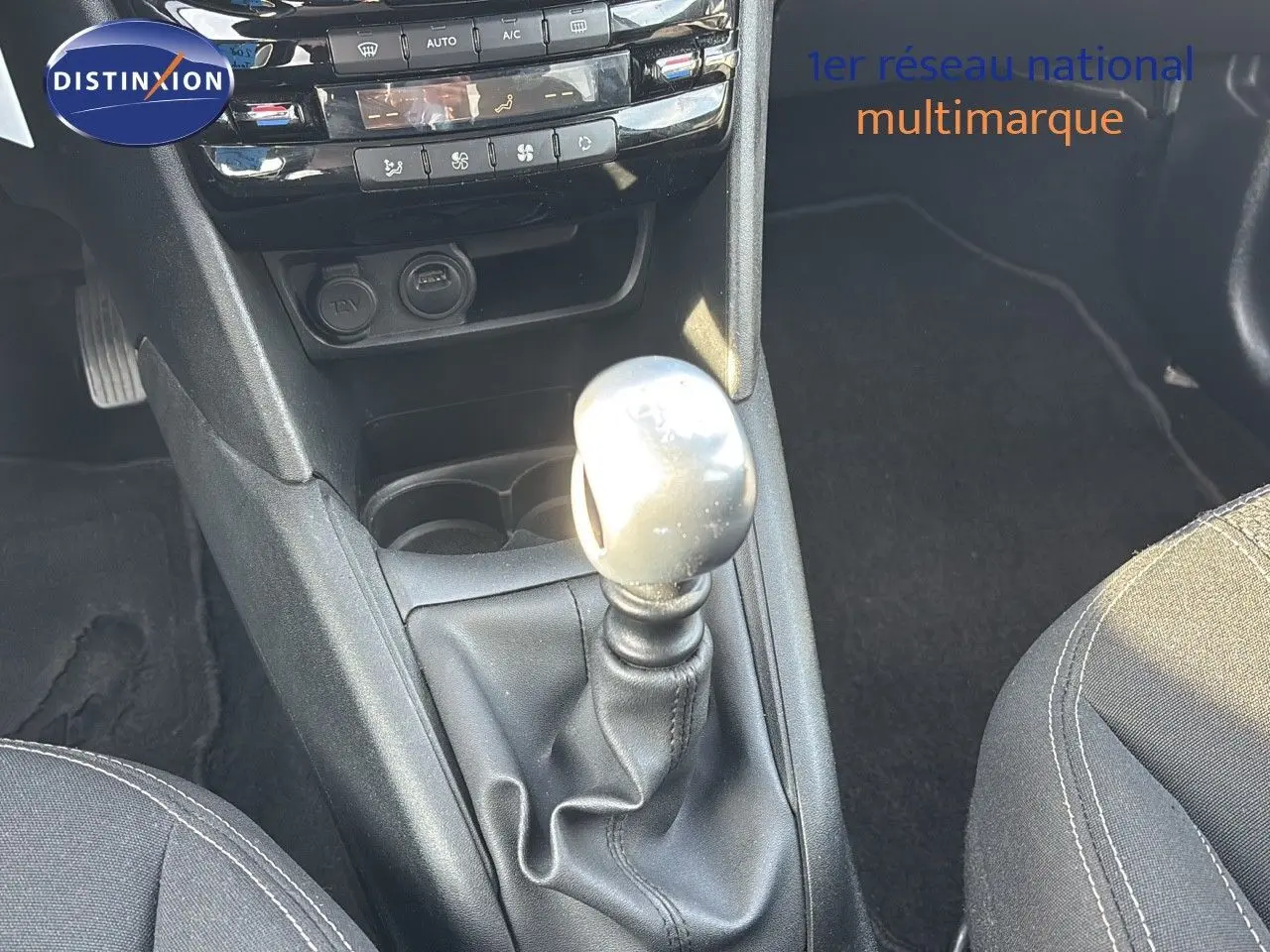 Le levier de vitesses manuel de la Peugeot 208 noir perle métal vu de dessus avec la console centrale et les sièges partiellement visibles.