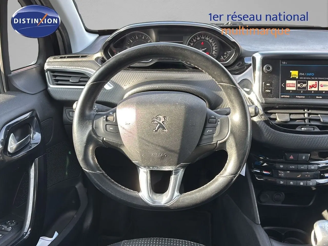 Vue intérieure centrée sur le volant Peugeot 208 1.2 PureTech noir, avec tableau de bord et écran tactile visibles.