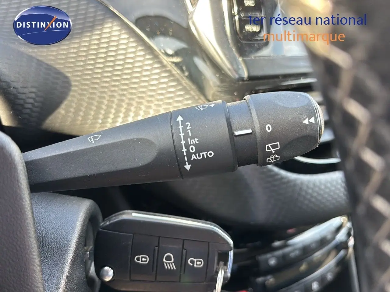 Gros plan sur la commande d'essuie-glace à gauche du volant dans l'habitacle d'une Peugeot 208 noire perle métal.