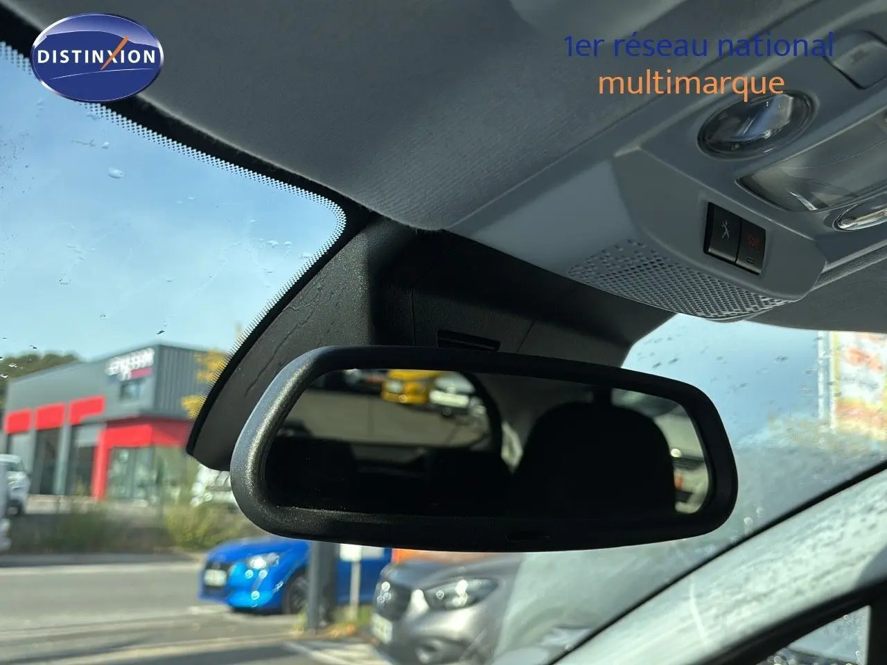 Rétroviseur intérieur d'une Peugeot 208 noire perle métal, avec vue floue sur des voitures en arrière-plan.