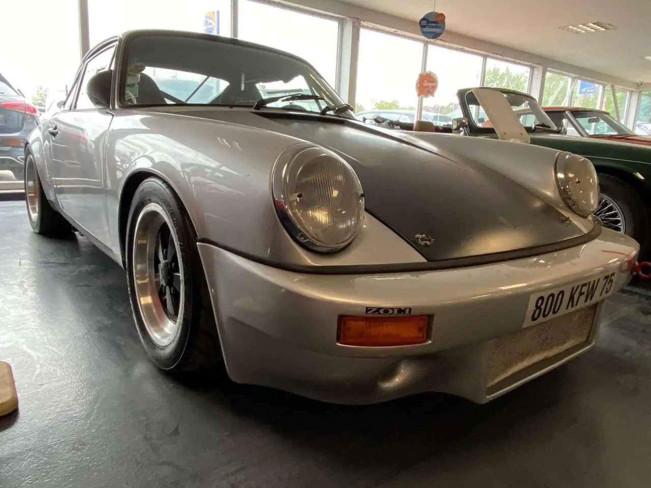 Porsche 911 3.0 SC gris métallisé vue 3/4 avant avec capot noir mat et jantes Fuchs noires.