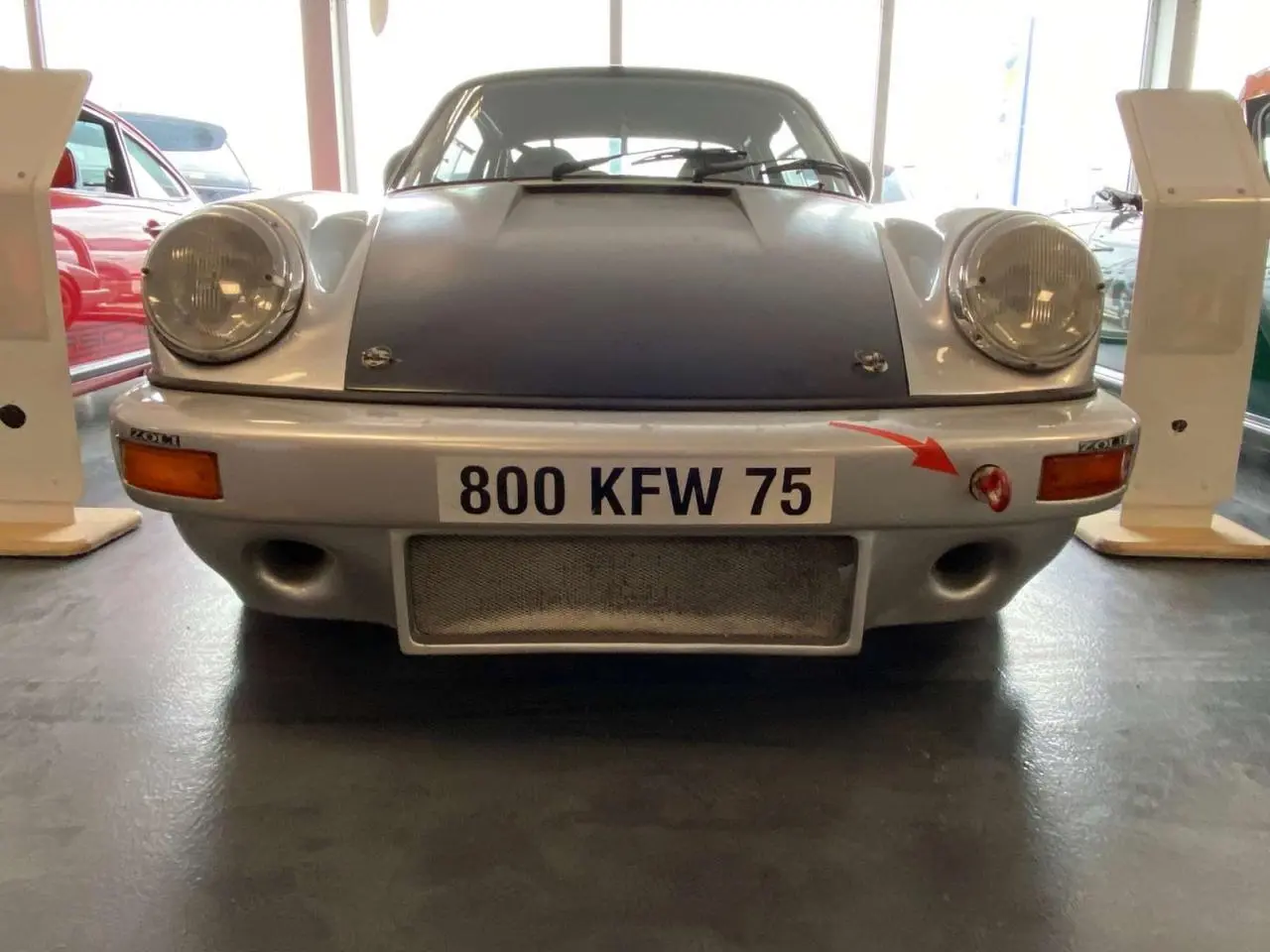 Vue frontale d'une Porsche 911 3.0 SC 930 gris métallisé avec capot noir mat et attache rouge sur pare-chocs.