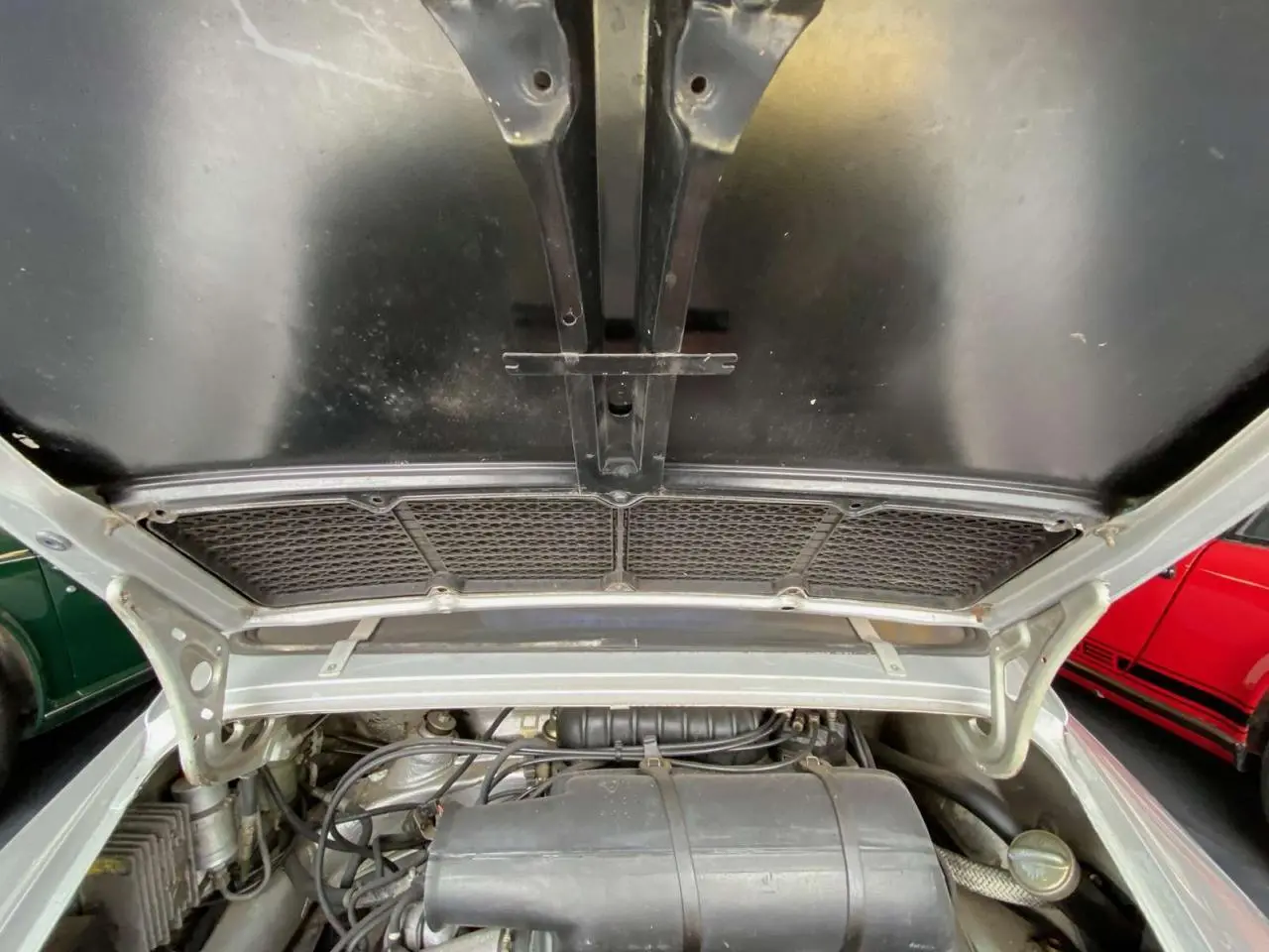 Moteur visible sous le capot ouvert d'une Porsche 911 3.0 SC gris métallisé, vue arrière rapprochée.