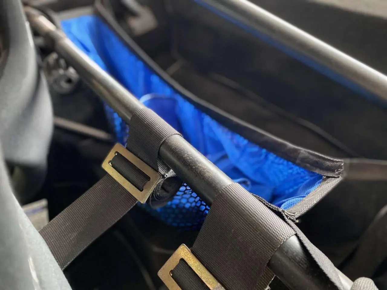 Détail intérieur montrant un filet porte-paquets bleu fixé à l'arceau tubulaire noir d'une Porsche 911 3.0 SC 1980.