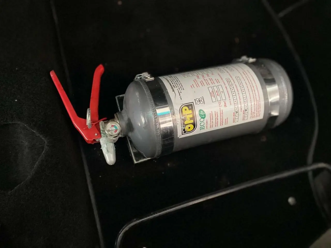 Extincteur gris avec poignée rouge posé sur le sol noir de l'habitacle d'une Porsche 911 3.0 SC 1980.