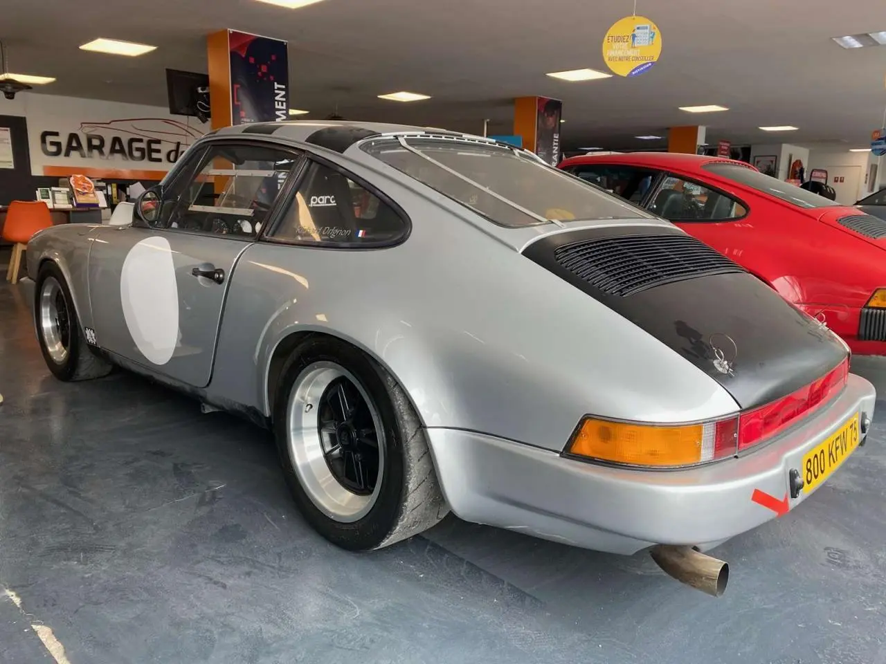 Vue 3/4 arrière droite d'une Porsche 911 3.0 SC gris métallisé avec jantes Fuchs et capot arrière noir mat.