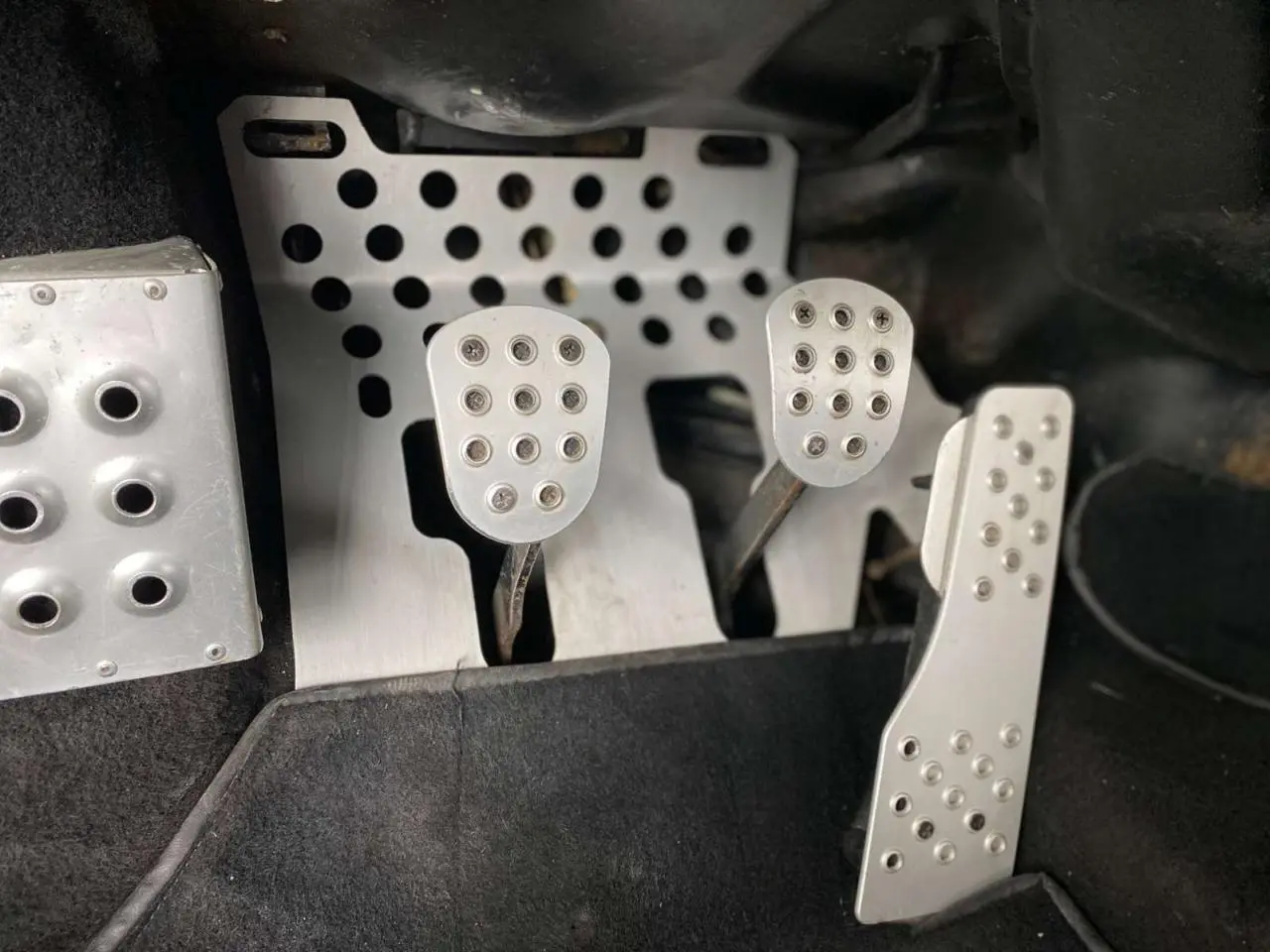 Gros plan sur les pédales en aluminium perforé d'une Porsche 911 3.0 SC 930 gris métallisé de 1980 avec boîte manuelle.