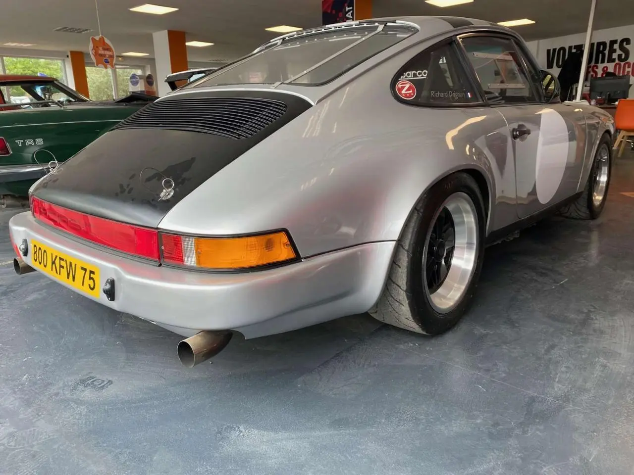 Vue 3/4 arrière droite d'une Porsche 911 3.0 SC gris métallisé avec jantes Fuchs et capot arrière noir mat.