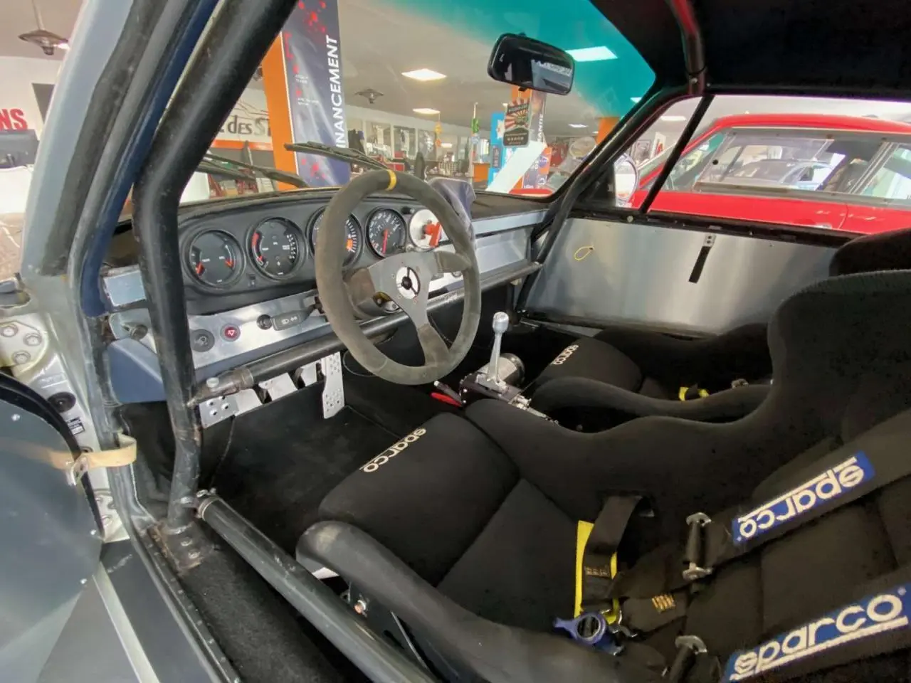 Intérieur côté conducteur d'une Porsche 911 3.0 SC gris métallisé avec baquets Sparco et arceau de sécurité.