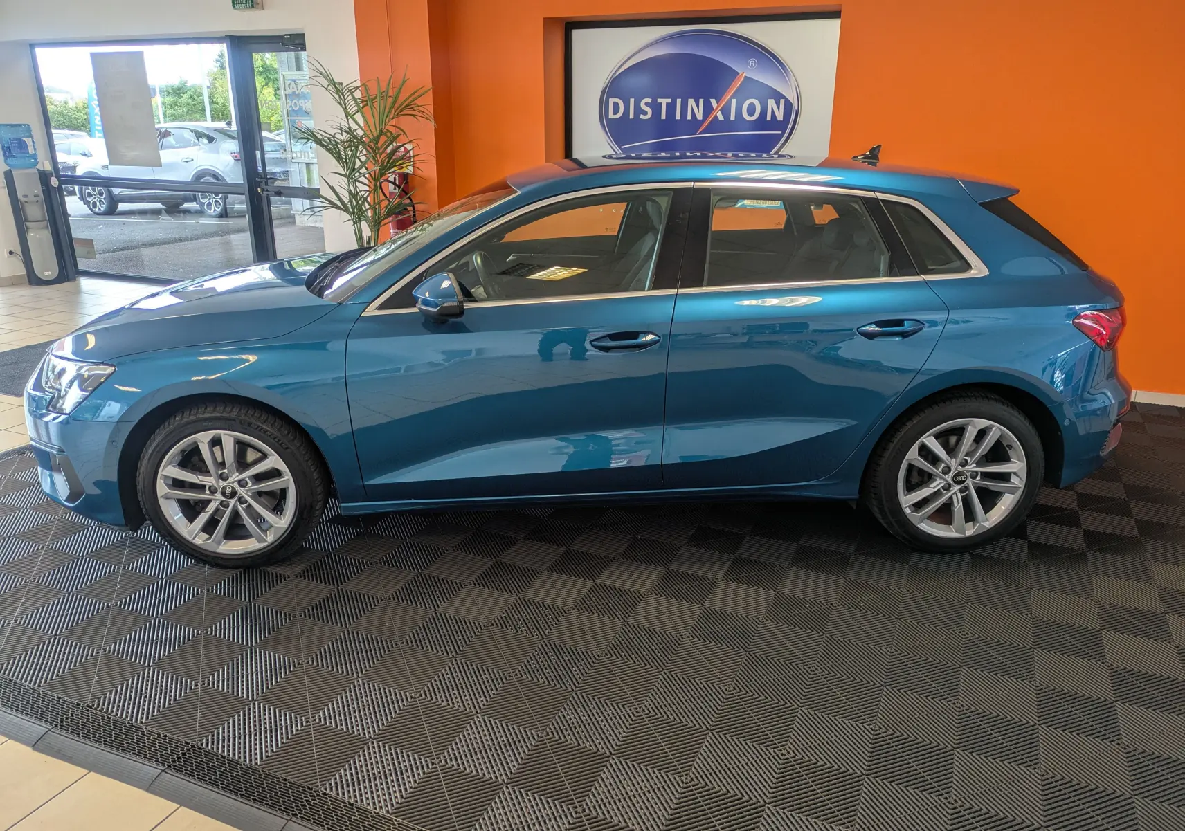 Profil côté gauche d'une Audi A3 Sportback bleu Atollblau metallic, exposée en intérieur avec jantes alliage 17 pouces.