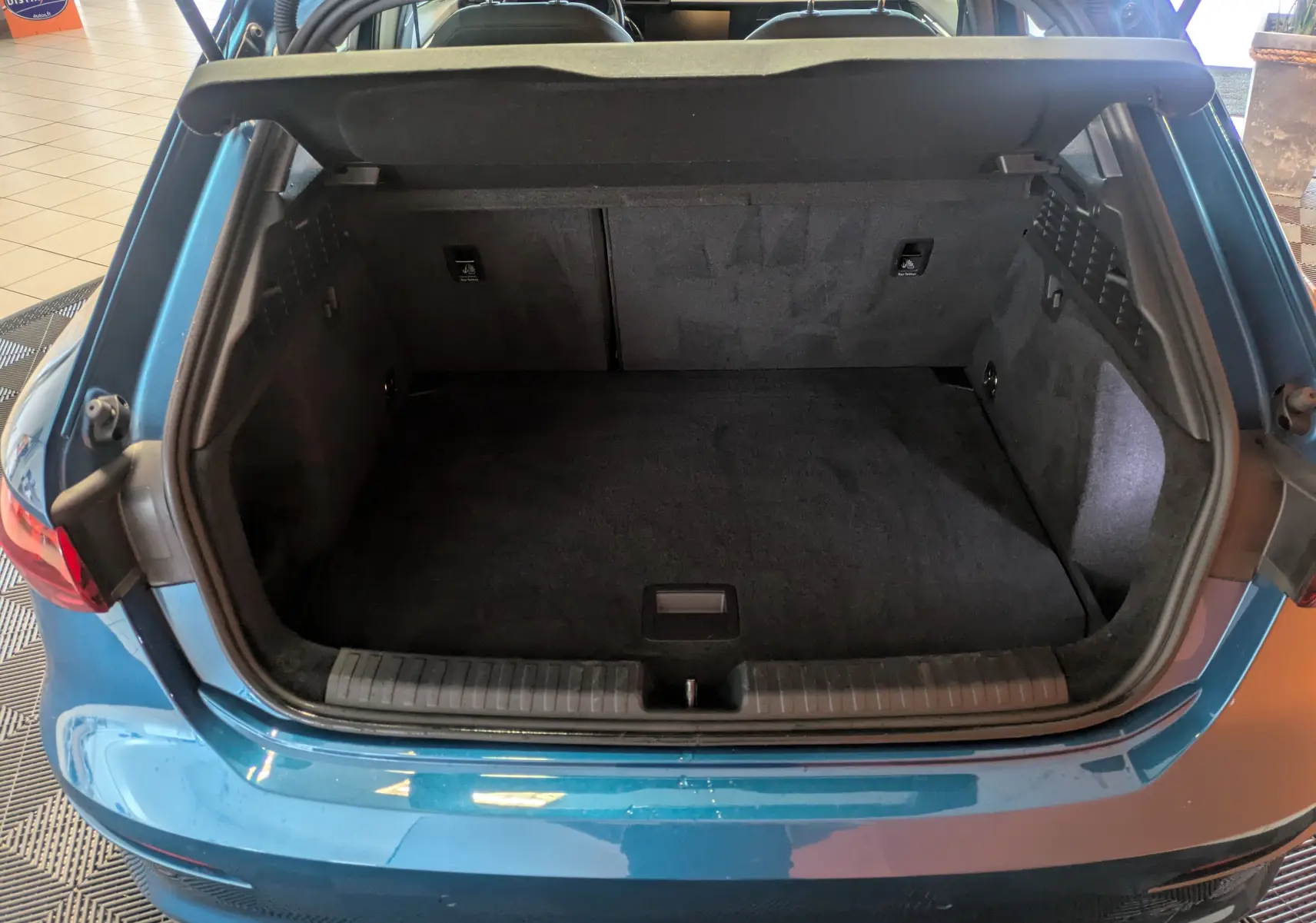 Coffre ouvert vu de l'arrière d'une Audi A3 Sportback bleu Atollblau, montrant l'espace de chargement vide.