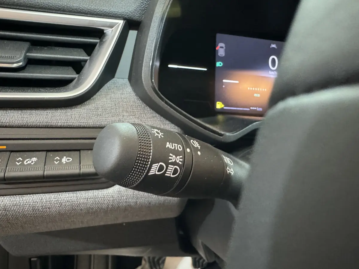 Gros plan sur la commande des phares à gauche du volant dans l'habitacle d'une Renault Clio gris clair 2025.