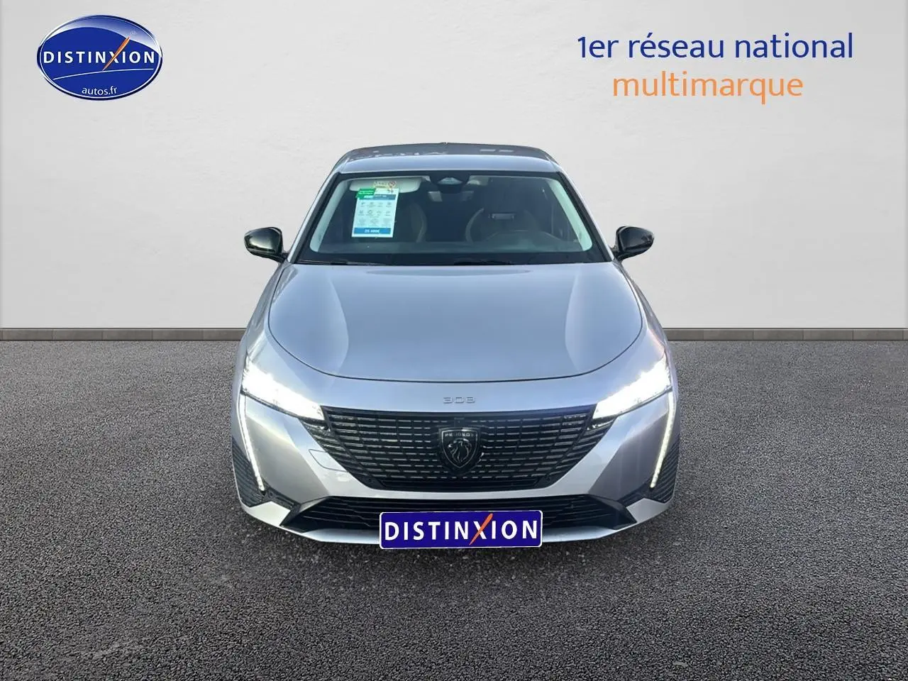 Vue avant d'une Peugeot 308 gris artense 2025 avec phares LED allumés et calandre noire distinctive.