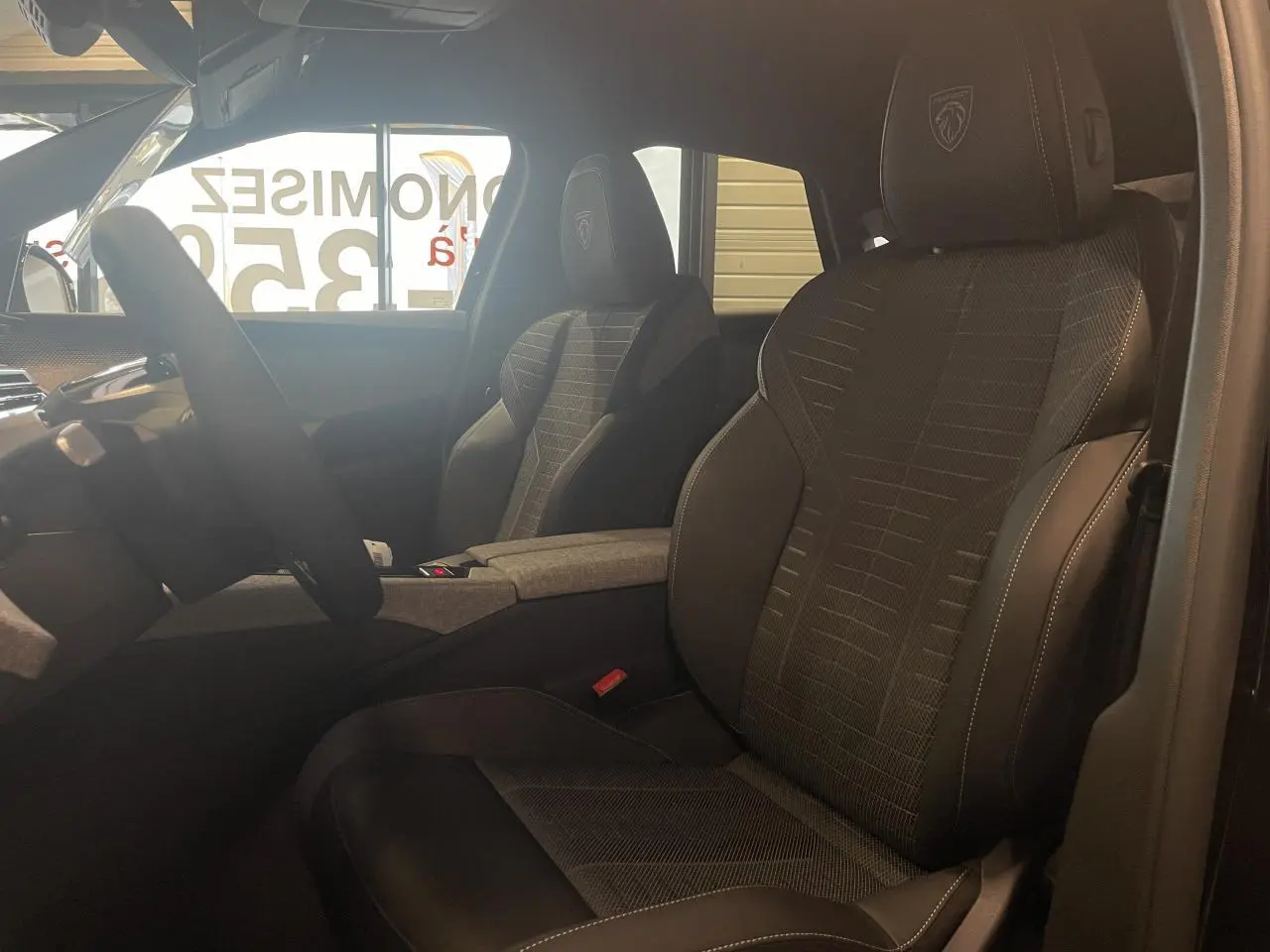 Vue intérieure côté conducteur du Peugeot 3008 2025, sièges tissu et cuir noir avec logo Peugeot brodé sur les appuie-têtes.