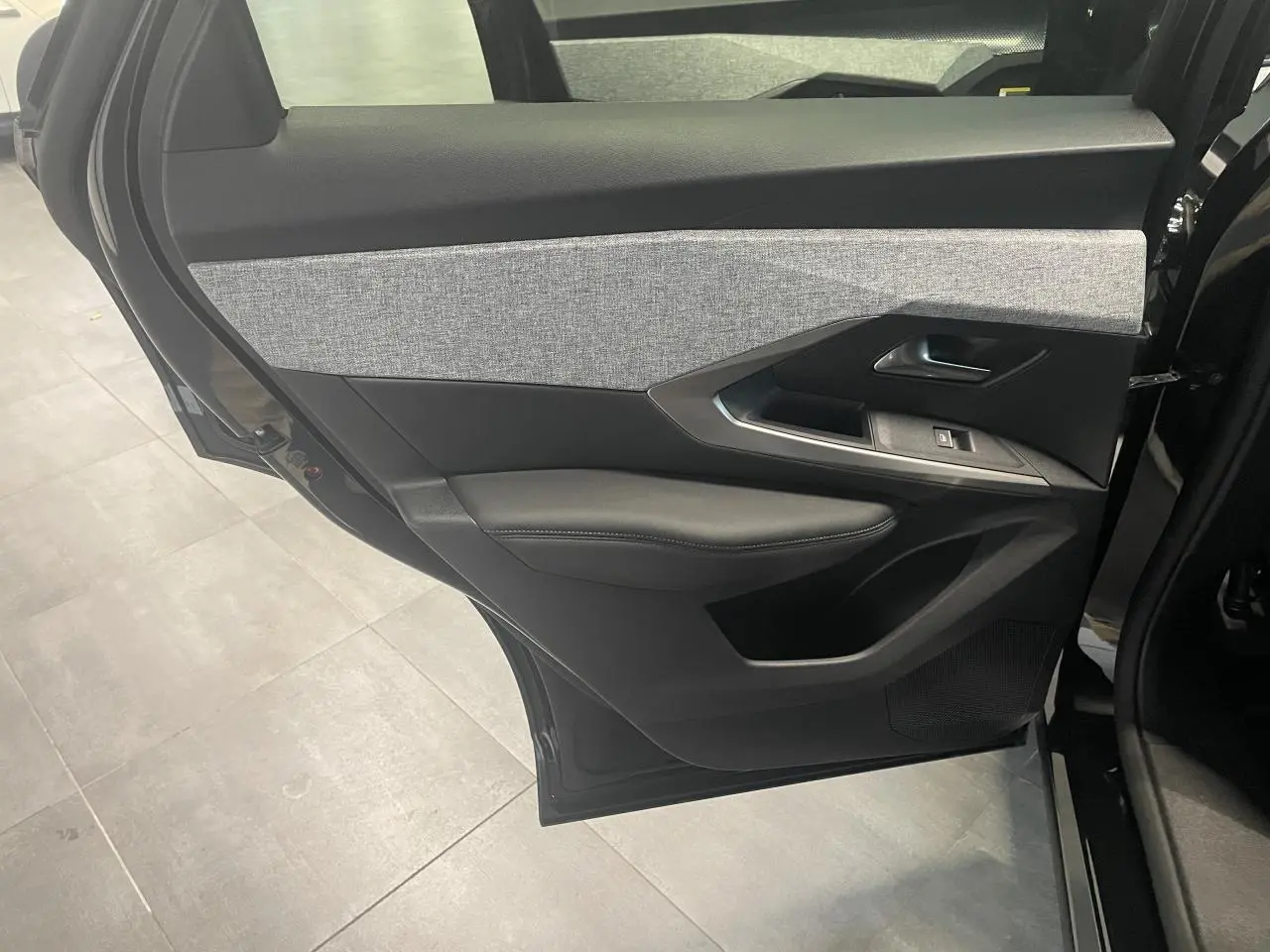 Vue intérieure du panneau de porte arrière gauche du Peugeot 3008 GT 2025 noir métallisé avec insert tissu gris et commandes de fenêtre.