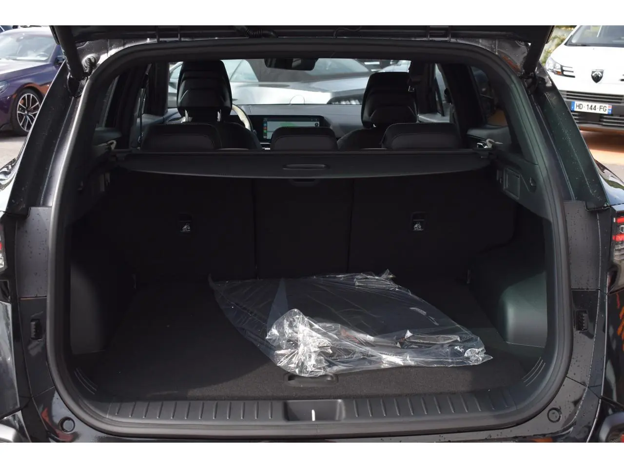 Coffre ouvert vu de l'arrière d'un KIA SPORTAGE noir 2026, avec intérieur spacieux et tapis plastique au sol.