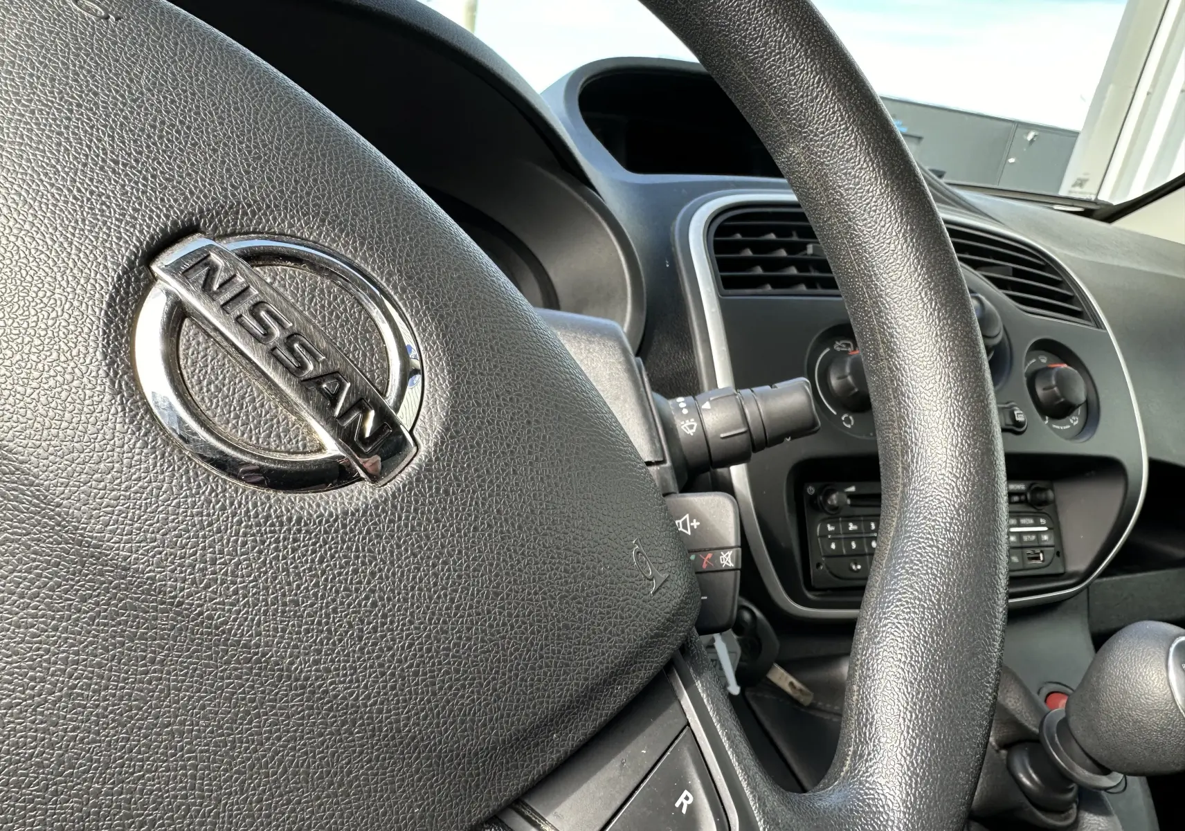 Gros plan sur le volant noir avec logo Nissan, tableau de bord et commandes centrales du Nissan NV250 blanc de 2020.