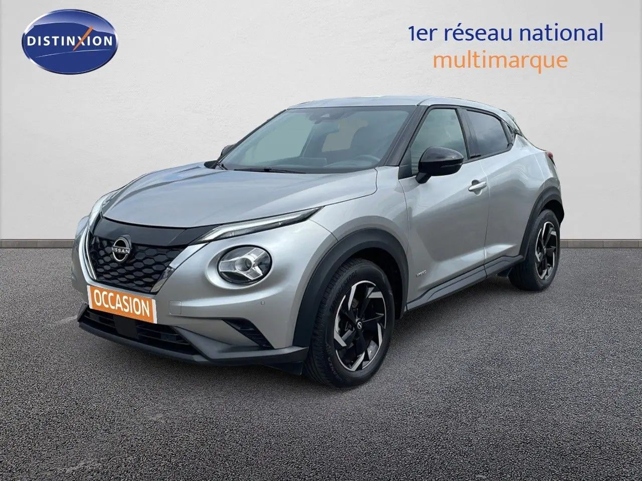 Nissan Juke Hybrid gris perle métal en 3/4 avant droit, avec jantes noires et calandre noire distinctive.