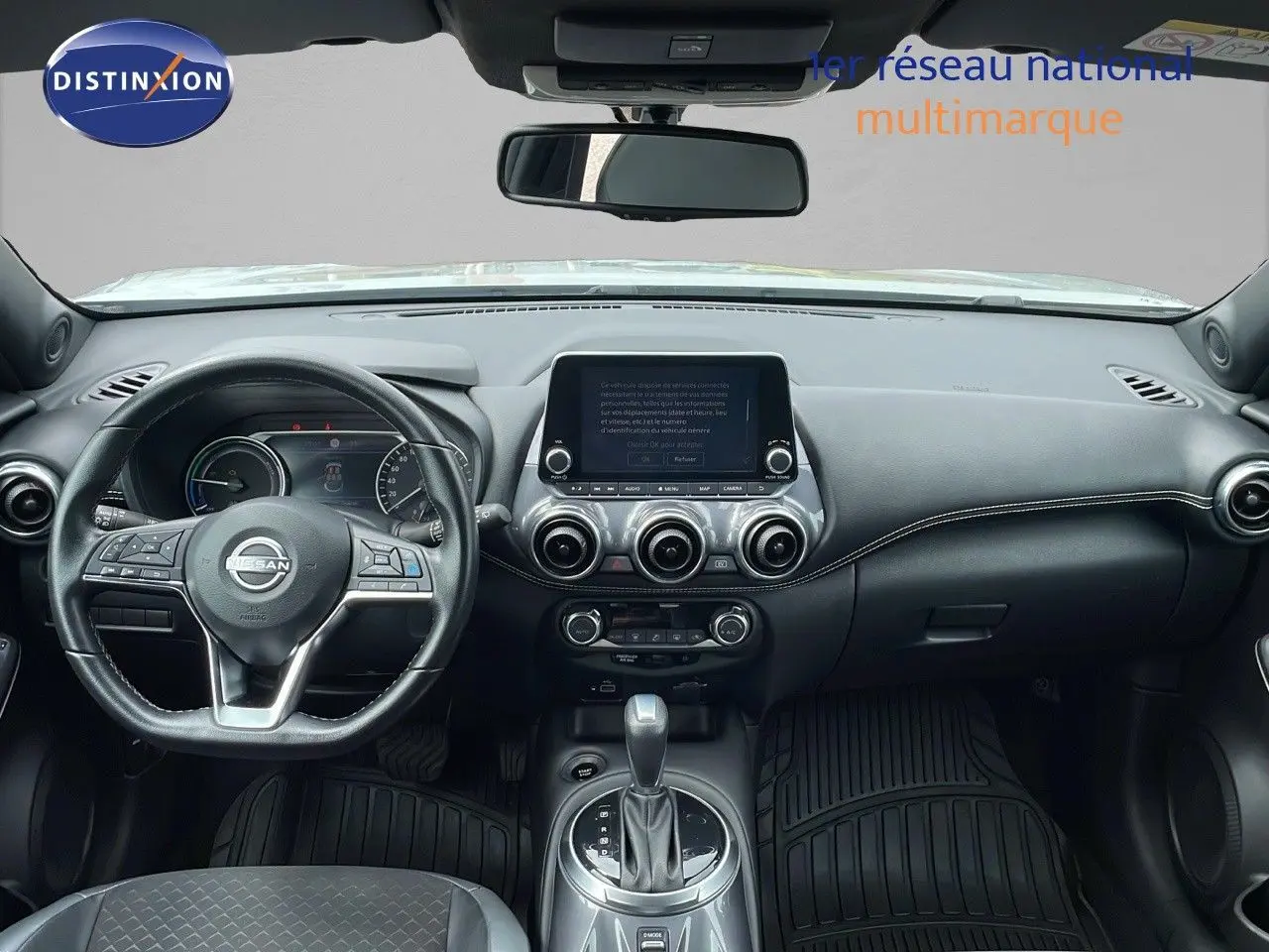 Intérieur noir du Nissan Juke Hybrid 2023 vu de face, tableau de bord moderne avec écran tactile central et volant multifonction.