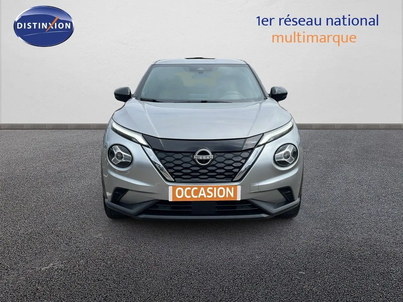 Vue frontale d'un Nissan Juke Hybrid gris perle métal avec calandre noire et phares ronds distinctifs.