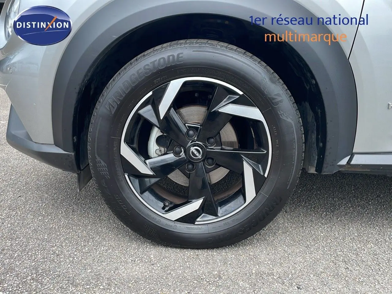 Gros plan sur la roue avant gauche d'un Nissan Juke Hybrid gris perle métal avec jante noire et argentée.