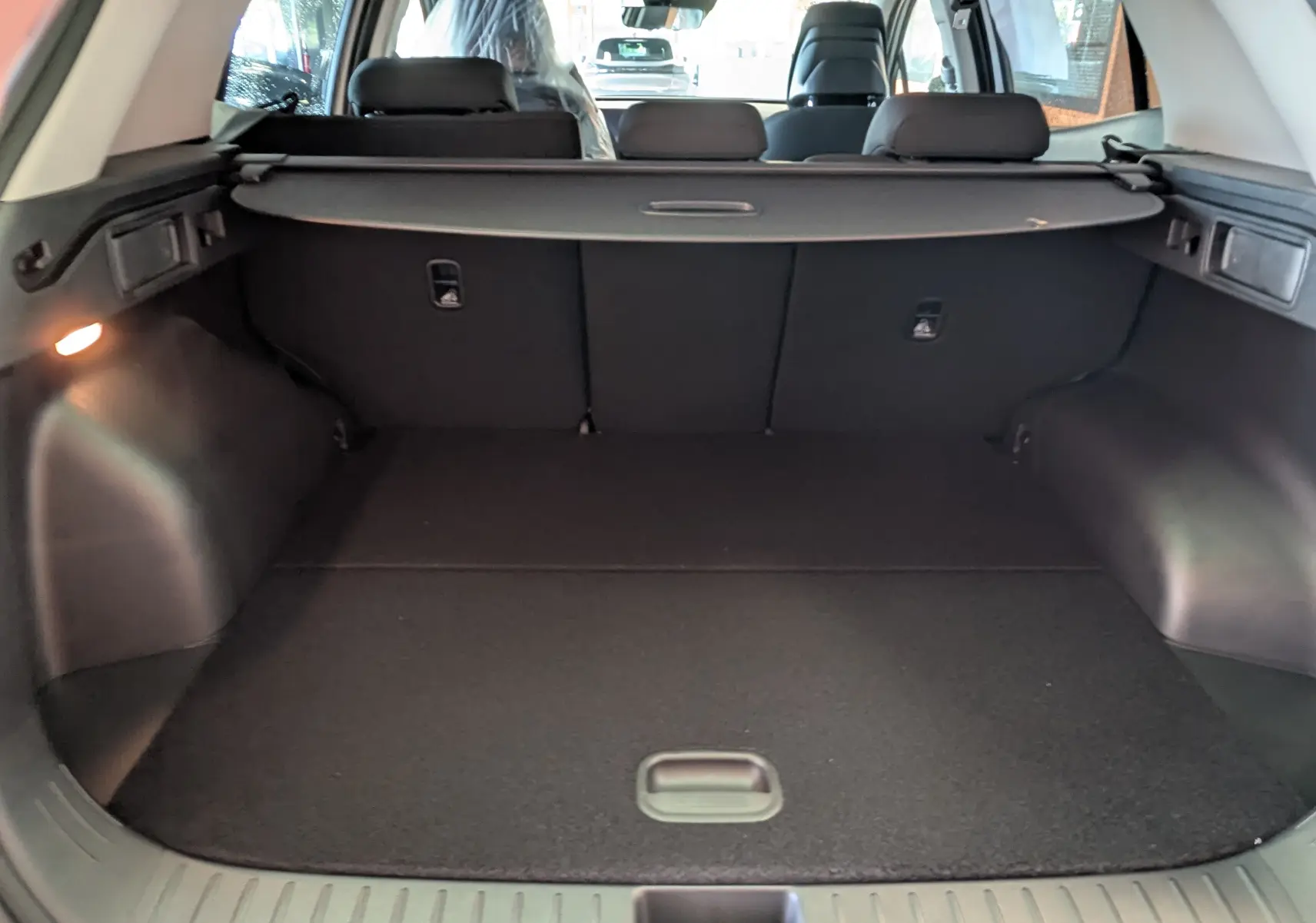 Coffre spacieux du Kia Sportage blanc MY25, vue intérieure arrière avec cache-bagages et banquette rabattue.