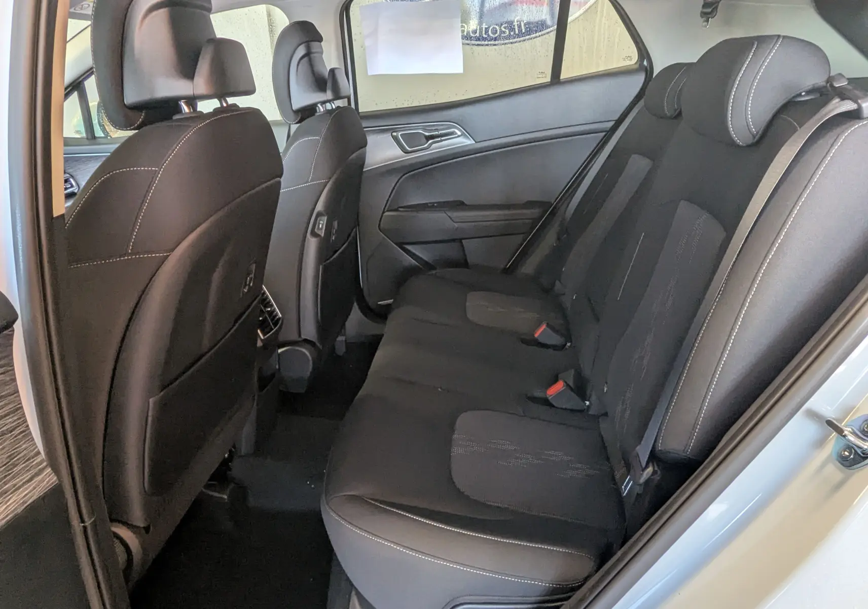 Vue latérale droite de l'intérieur arrière du Kia Sportage blanc 2025, sièges noirs avec surpiqûres blanches et ceintures rouges.